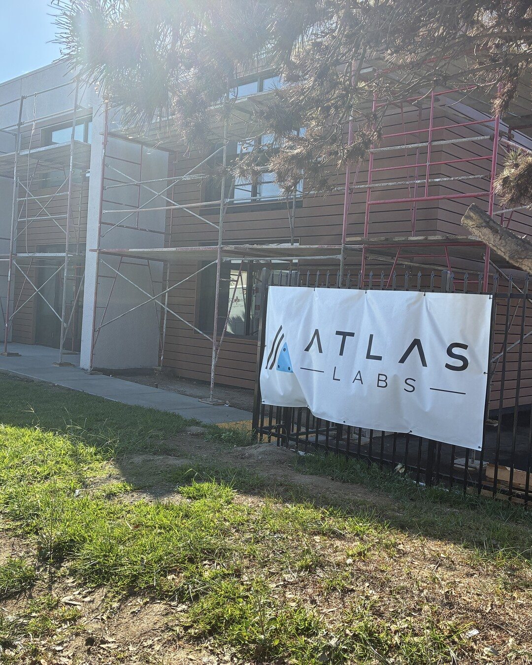 The Atlas Labs banner hung on the fence in front of the building, with new wood-slat siding and scaffolding behind it.