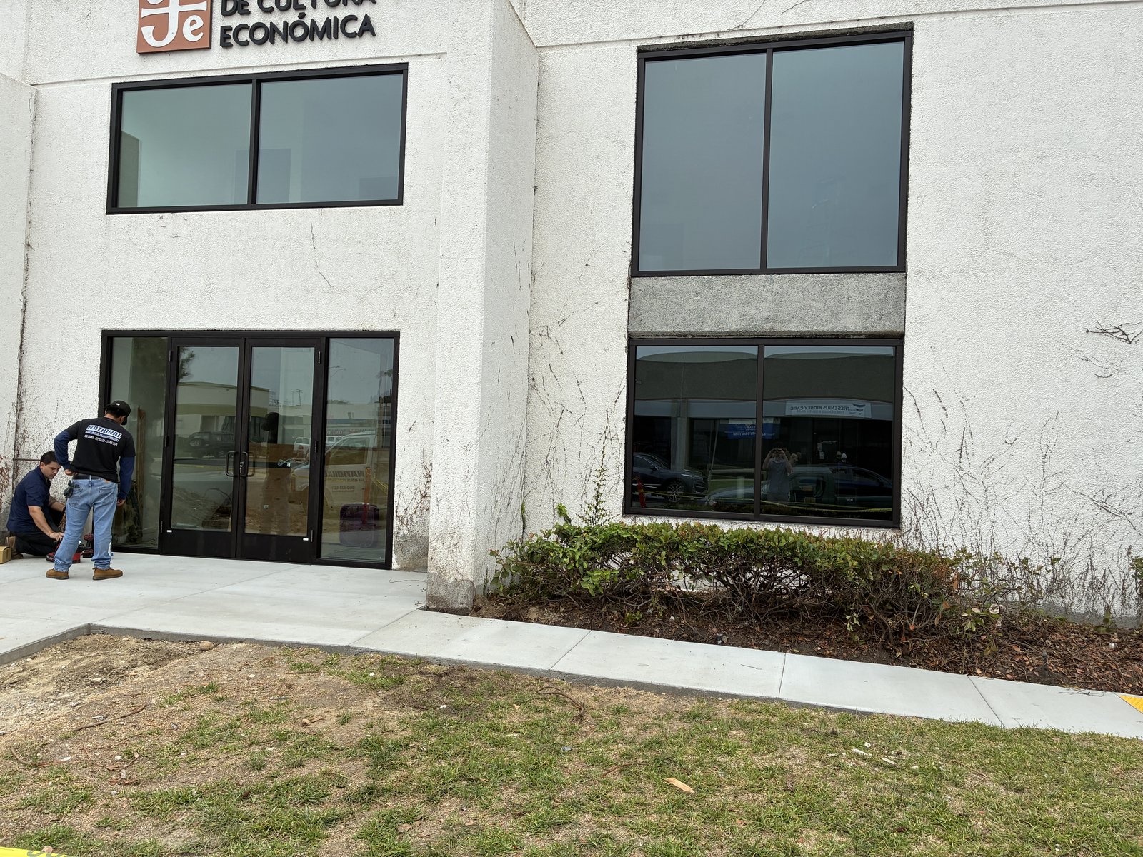 New black-framed storefront doors installed along the front of the building, with a fresh concrete walkway.