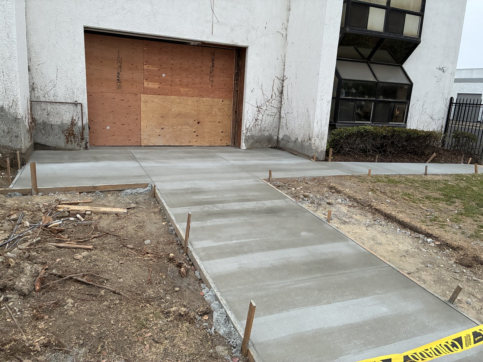 Freshly poured concrete slab and walkway at the main shop entrance, with the roll-up door opening framed and boarded over.