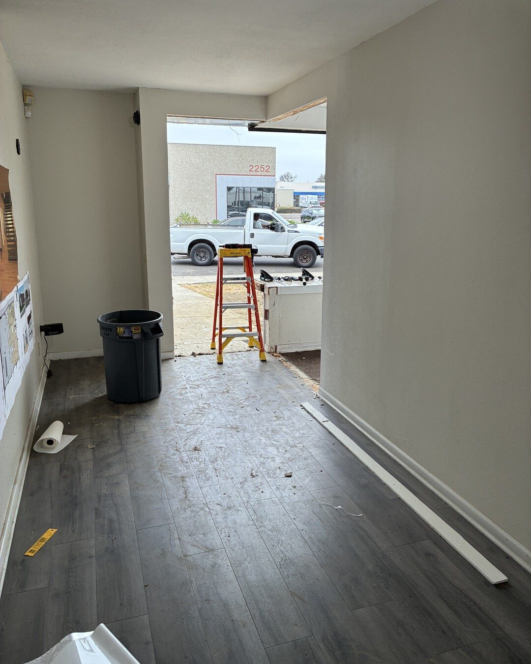 First look inside the ground floor during demolition: gray wood-look flooring, bare walls, and a new opening cut through to the street.